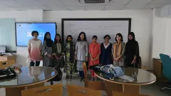Participants of the BDOAA Women's Astronomy Olympiad Preparation Camp standing with an instructor in front of a whiteboard covered in blackbody and spectral energy distribution notes.