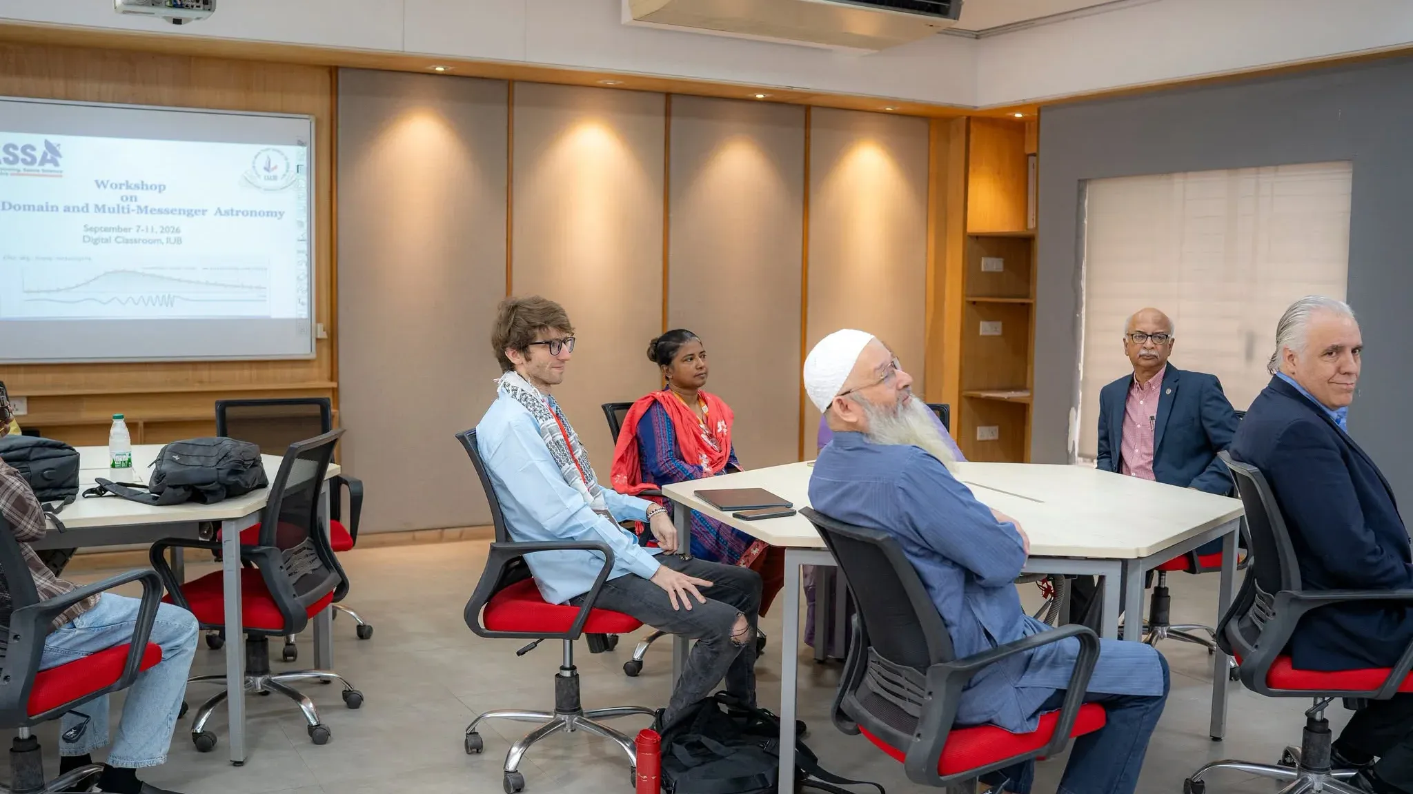Dr. Andrew L. Miller, in a denim shirt and scarf, sits at left among guests at the front table of the Digital Classroom.