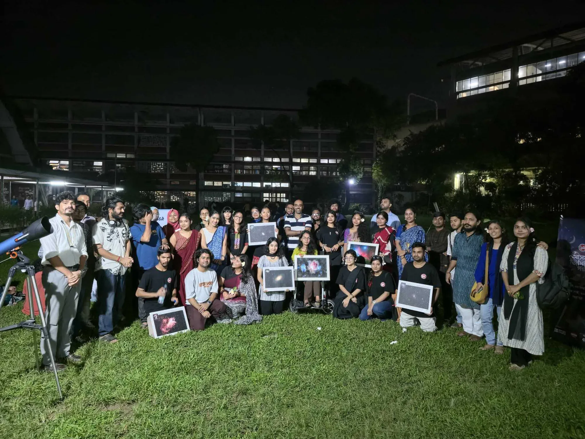 Participants and Durbin volunteers gathered on the TSC lawn at night, several holding framed astrophotographs, with a telescope at the left of the frame.