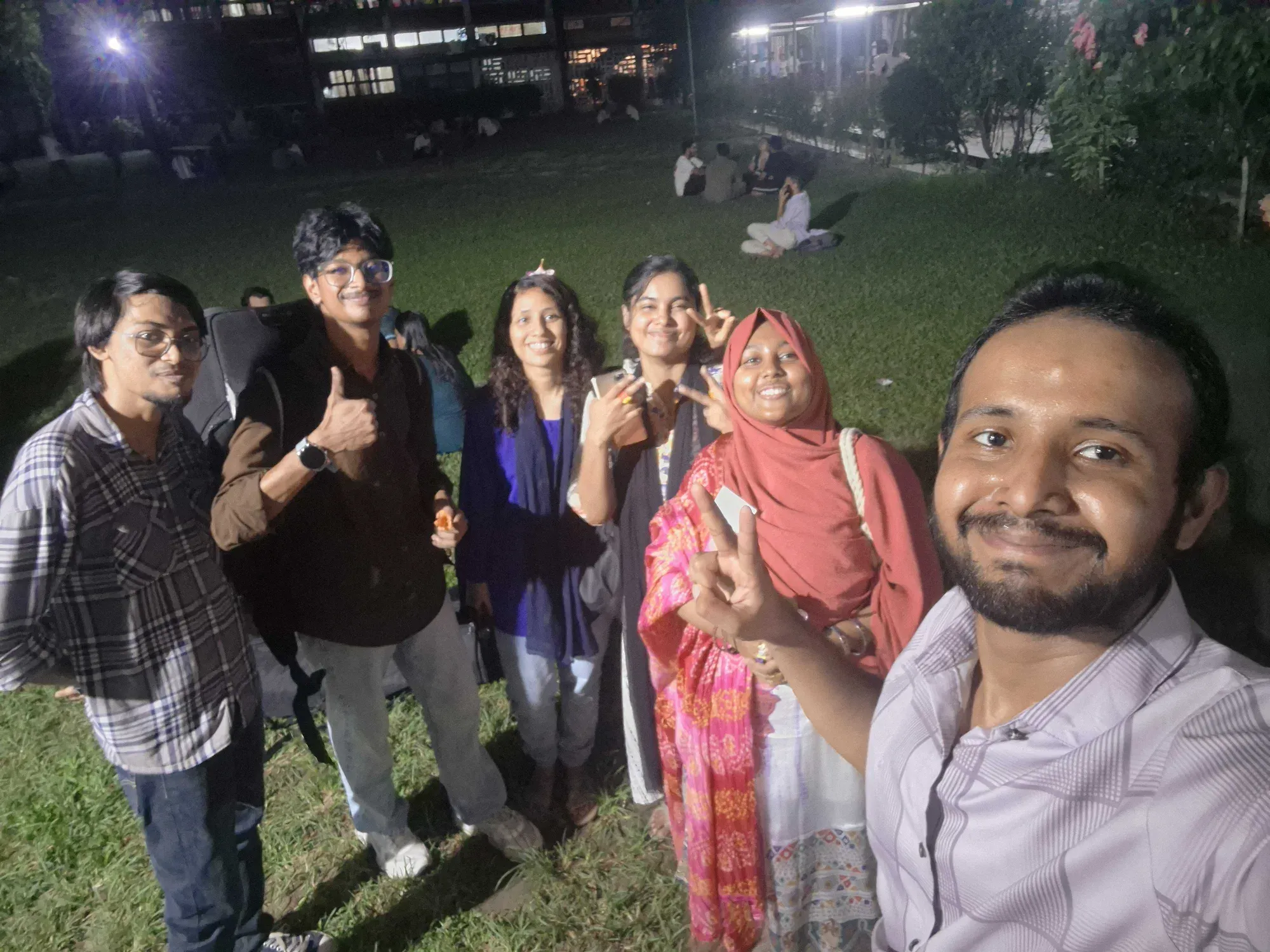 Six members of the Durbin and Bhoirobee teams standing together on the TSC lawn at night, smiling at the camera.