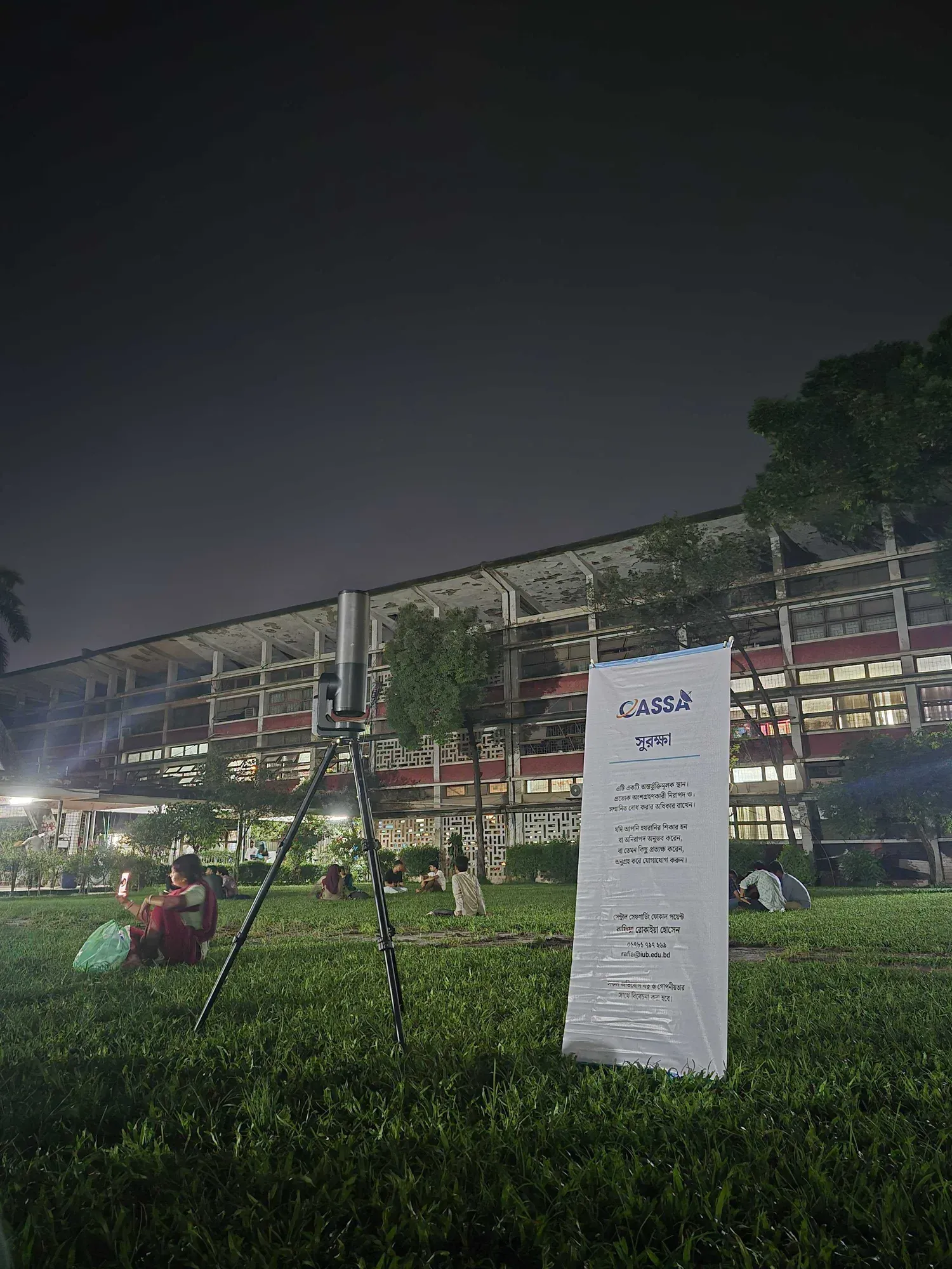 A telescope on a tripod beside a CASSA safeguarding banner on the TSC lawn, under a completely overcast night sky.