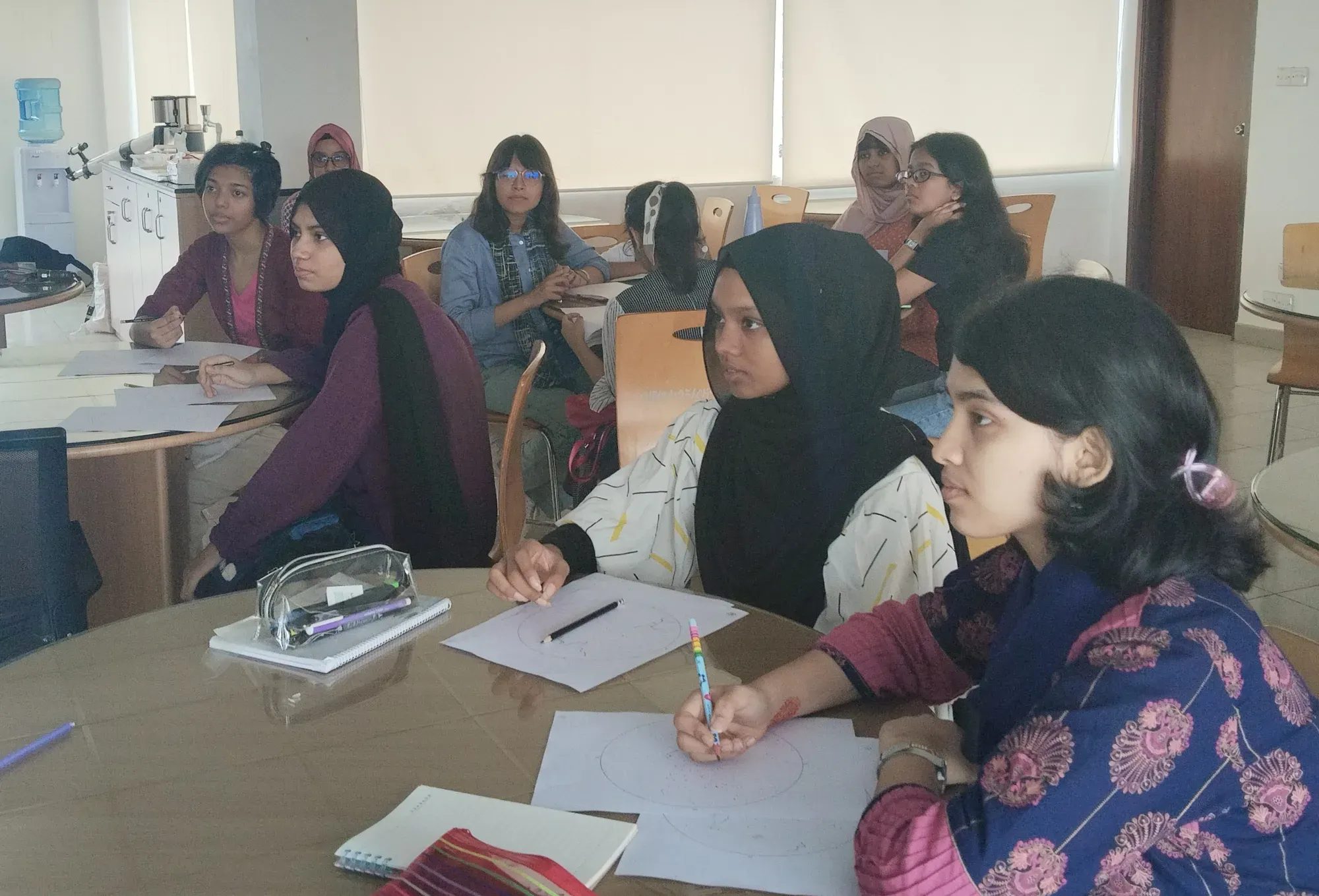 Participants seated around tables with skymap sheets and pencils in front of them, listening to a session.